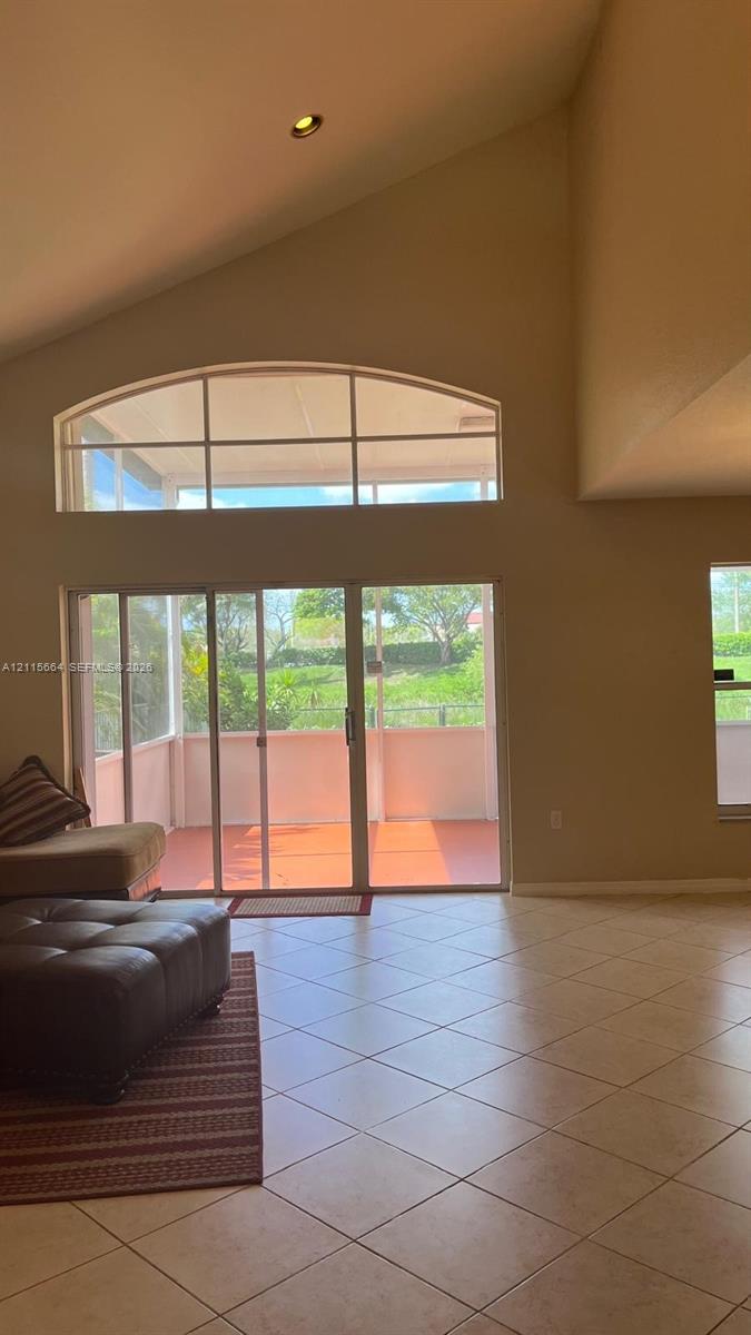 Vaulted ceiling with recessed lighting, tile flooring, and a large arched transom window above sliding glass doors