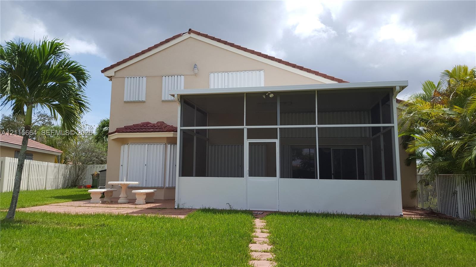 Two-story stucco exterior featuring a screened-in lanai, concrete paver patio, and attached metal storm shutters