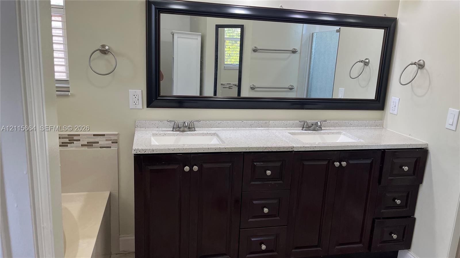 Double vanity featuring a dark-finish wood cabinet, light-toned stone-composite countertop, dual undermount sinks, and an expansive framed mirror