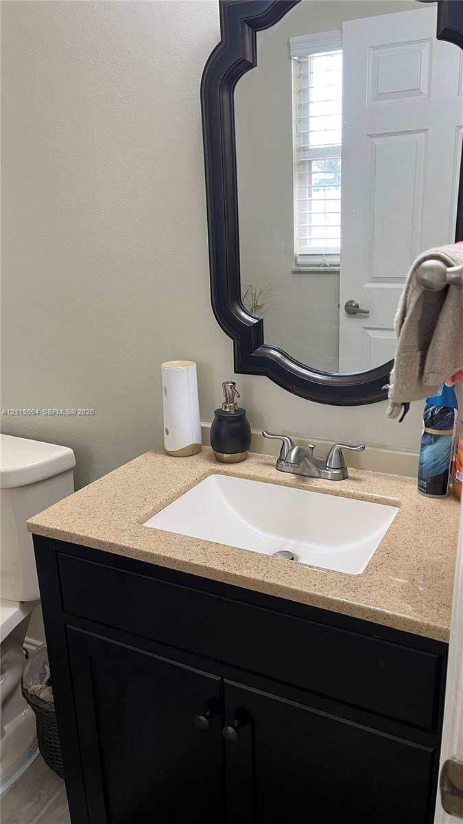 Black vanity cabinet featuring a solid-surface countertop with an integrated rectangular basin, two-handle faucet, and decorative framed mirror