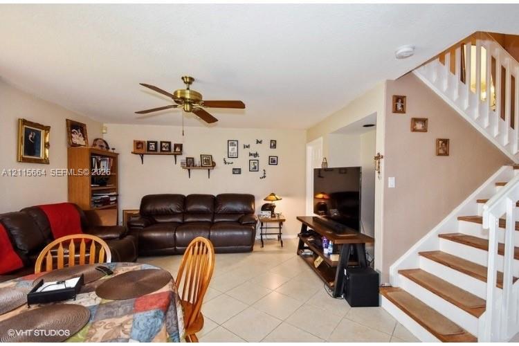 Open-concept floor plan featuring neutral tile flooring, a multi-blade ceiling fan, and a staircase with white balusters and wood-finished treads