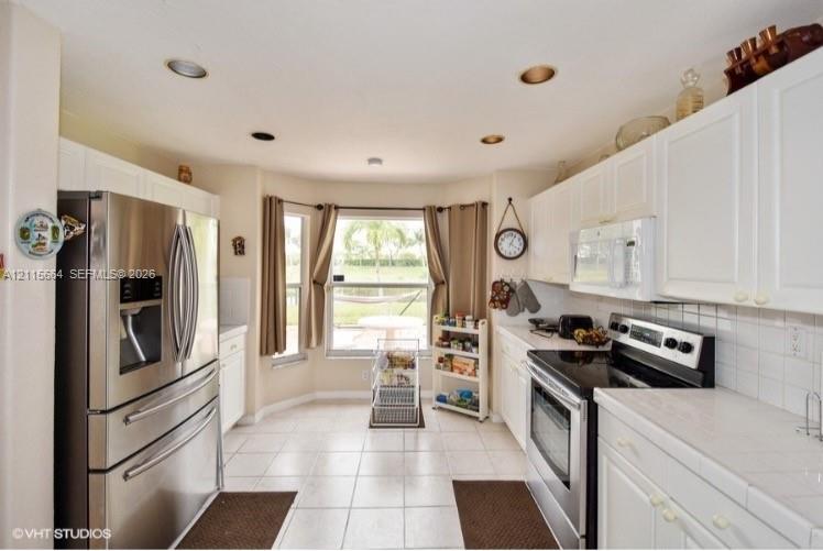 Kitchen featuring white cabinetry, tile countertops, stainless steel appliances, recessed lighting, and a bay window