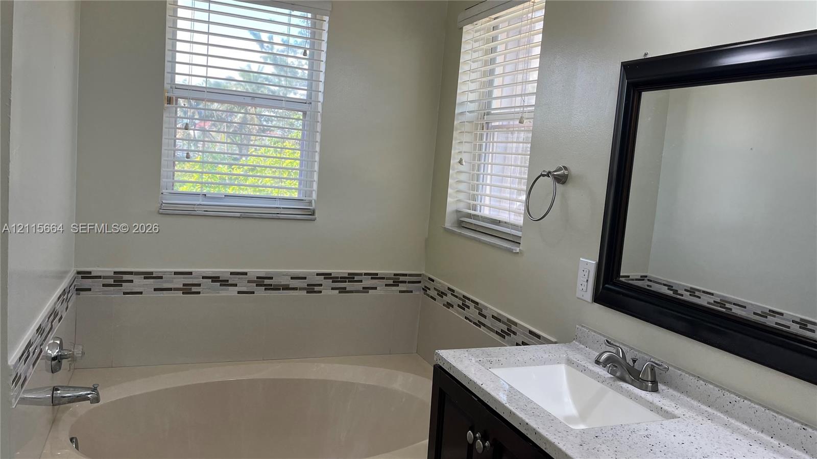 Bathroom featuring a deep oval soaking tub, custom tile backsplash, solid-surface countertop with integrated sink, and dual windows