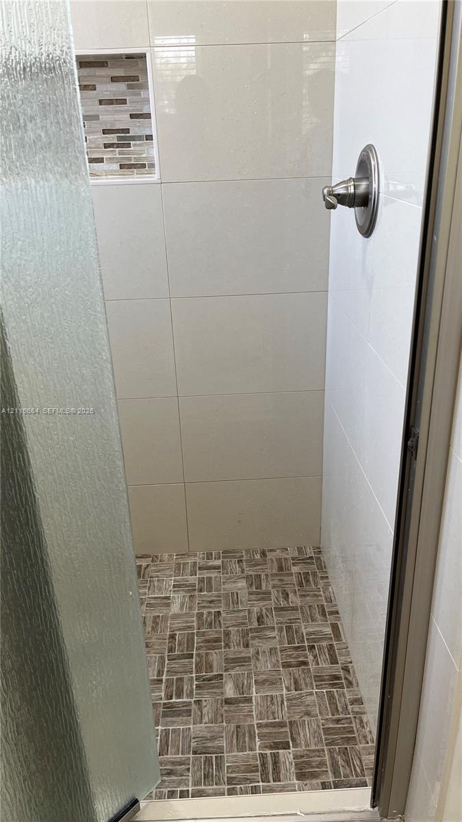 Shower stall featuring large-format wall tile, a mosaic tile niche, decorative stone-patterned floor tile, and a brushed-nickel shower handle