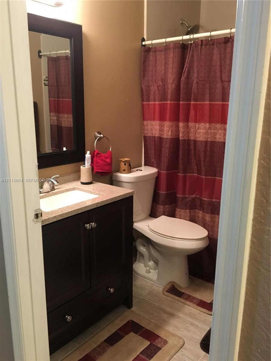 Bathroom featuring a dark wood-finish vanity with an integrated basin, stone-composite countertop, matching framed wall mirror, and tile flooring