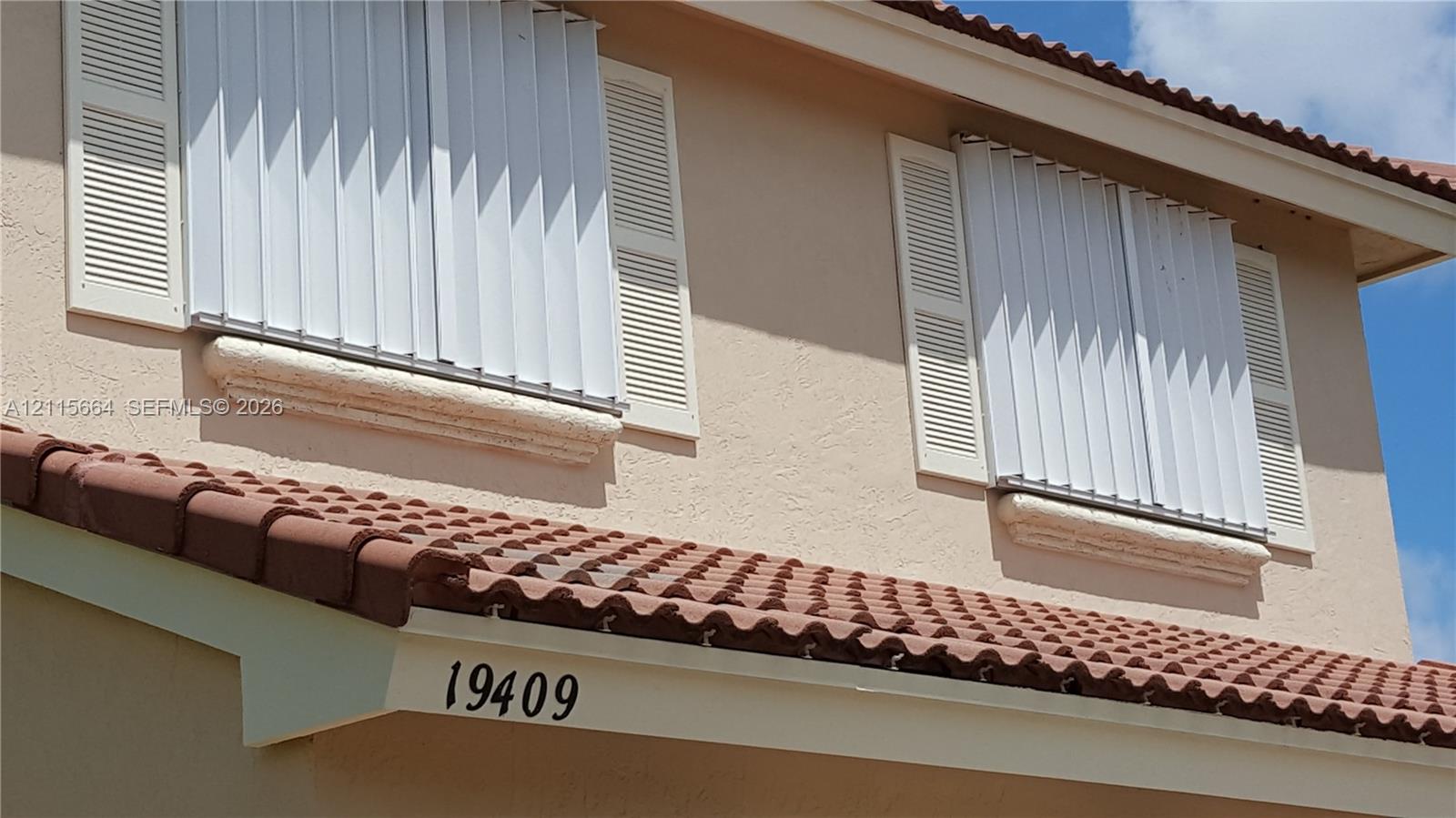 Exterior facade featuring a stucco finish, multi-level terra cotta tile roofing, louvered shutters, and metal storm shutters