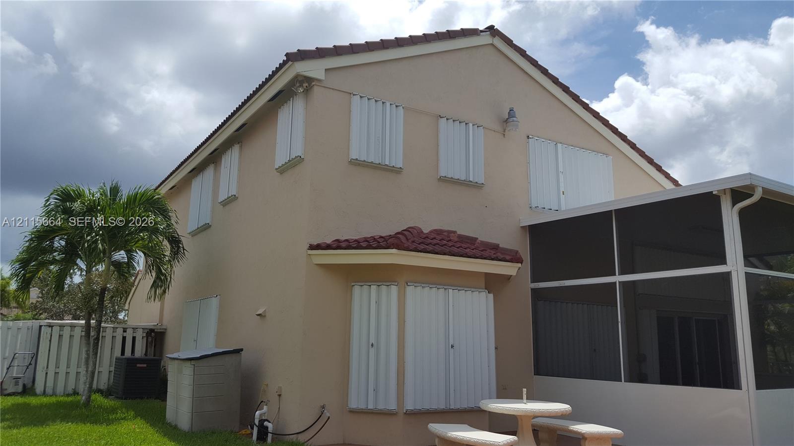 Stucco exterior featuring a multi-gable roof line with red tile accents, installed storm shutters, and an enclosed screen lanai