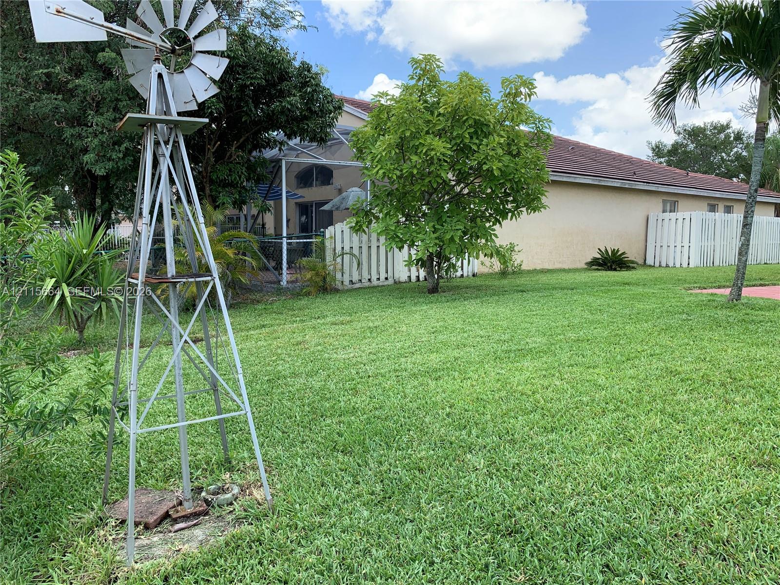 Expansive backyard featuring a metal windmill, white vinyl privacy fencing, a covered screened-in patio, and mature landscaping