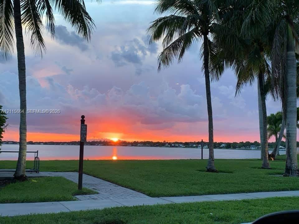 Waterfront property featuring manicured lawn, established palm trees, paved walkway, and direct water access
