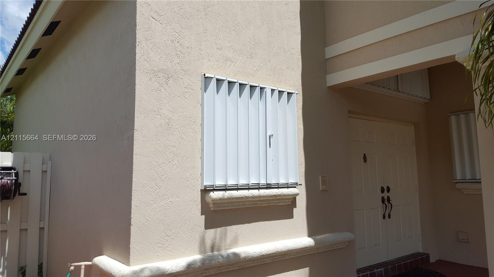 Stucco exterior featuring dual entry doors, metallic storm shutters, and decorative horizontal masonry trim