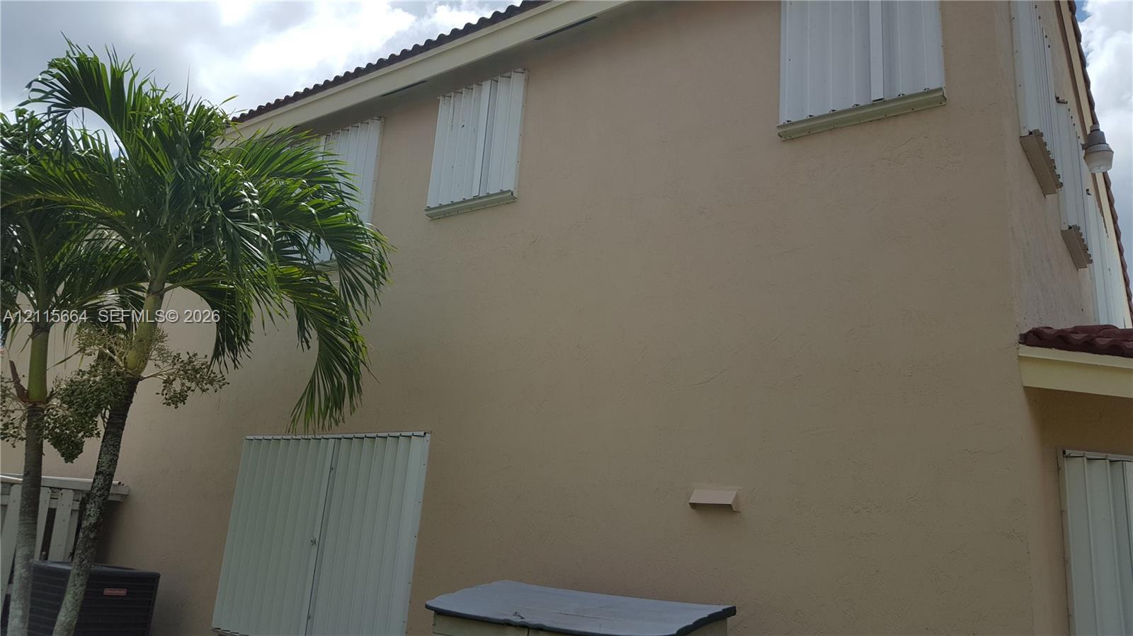Two-story exterior featuring a stucco facade, tile roof, and installed metal hurricane shutters