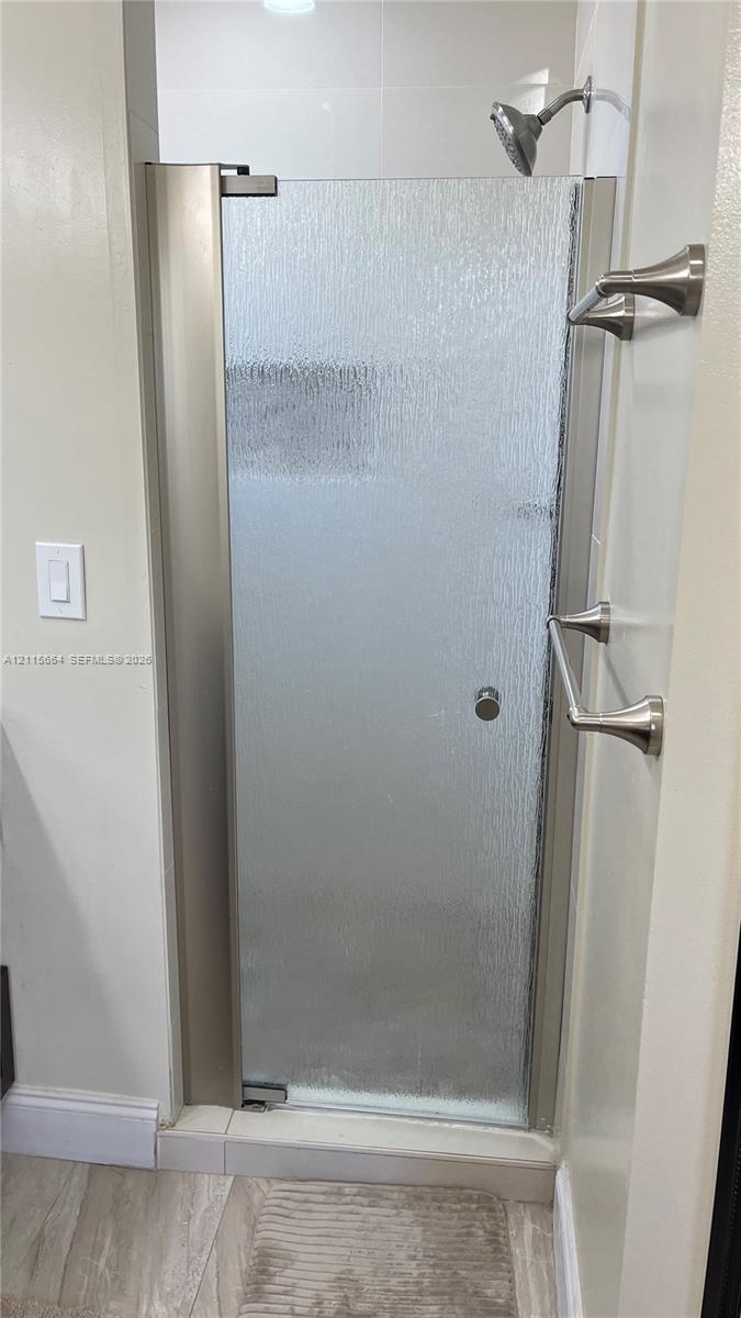 Shower enclosure featuring textured glass, a metal-finish frame, a wall-mounted shower head, and dual metal-finish wall-mounted towel bars