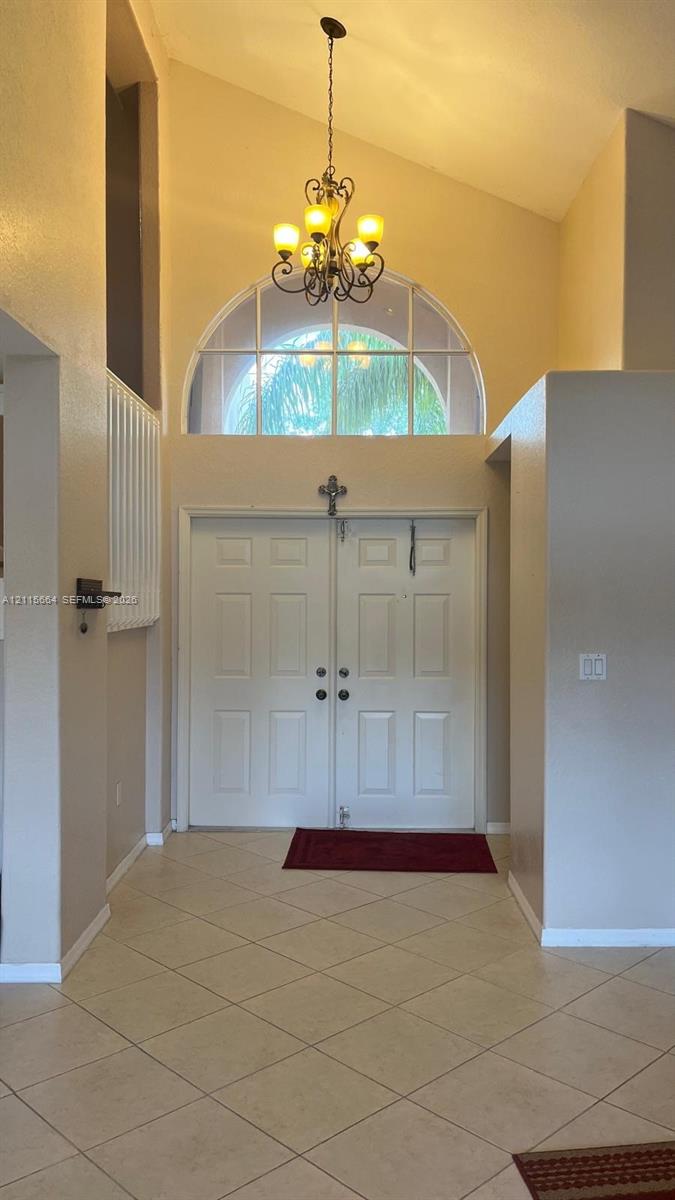 Double-entry doors featuring an arched transom window, vaulted ceiling, tile flooring, and a multi-light chandelier