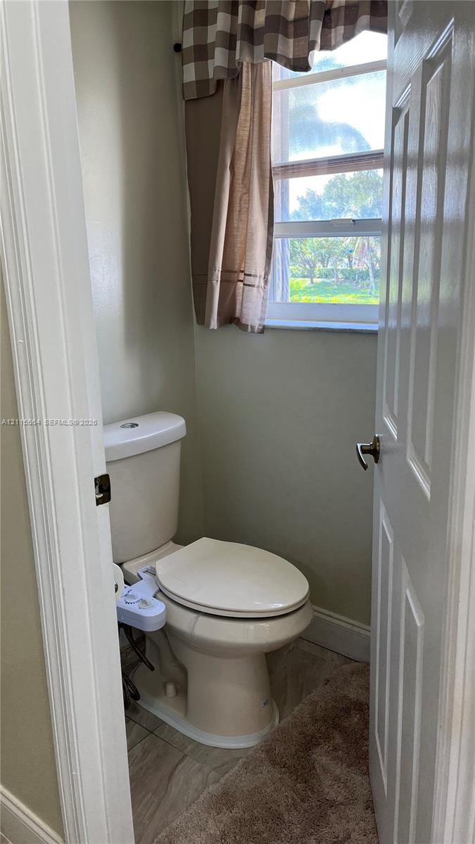 Neutral-toned bathroom featuring a two-piece elongated toilet, single-hung window, and tile flooring