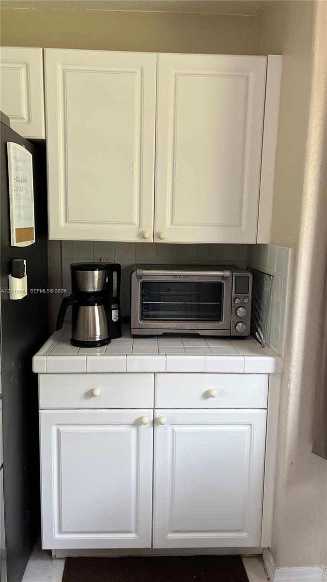 White cabinetry with traditional recessed-panel doors, square ceramic tile countertops, and integrated tile backsplash