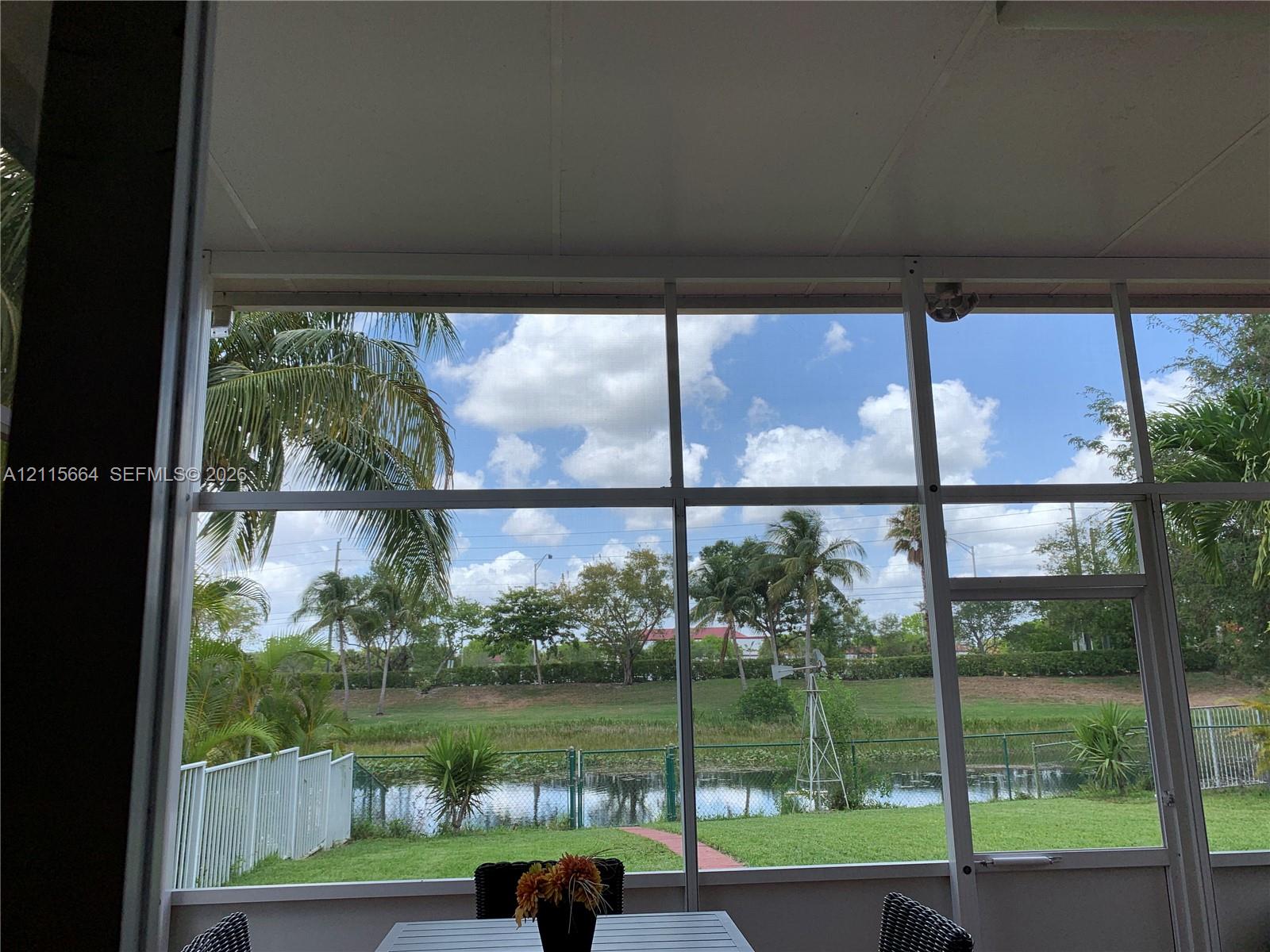 Screened-in patio featuring a white frame enclosure, metal ceiling, and a direct line of sight to a pond and manicured lawn