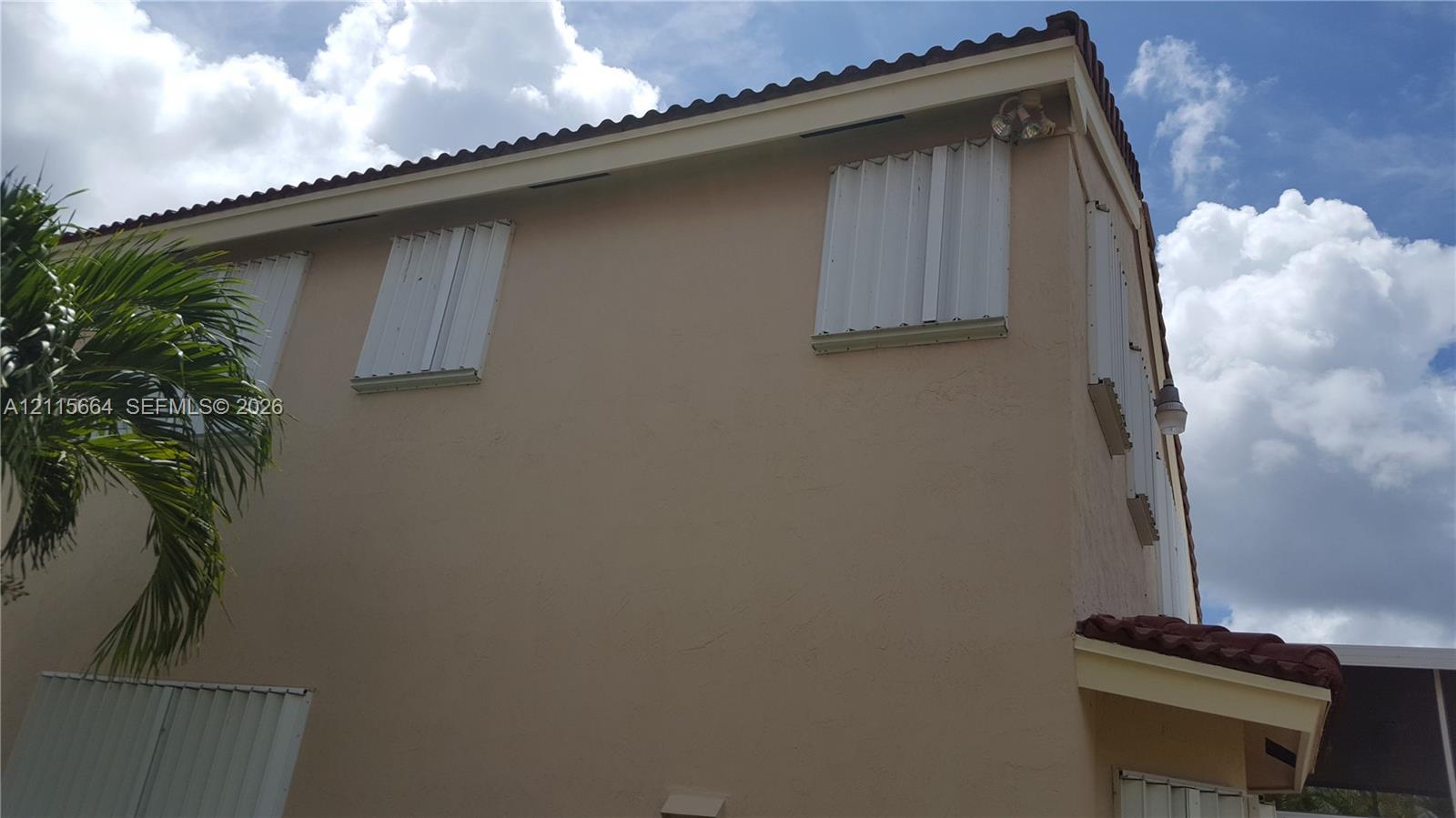 Exterior wall featuring smooth stucco finish, barrel tile roofline, and installed metal storm shutters