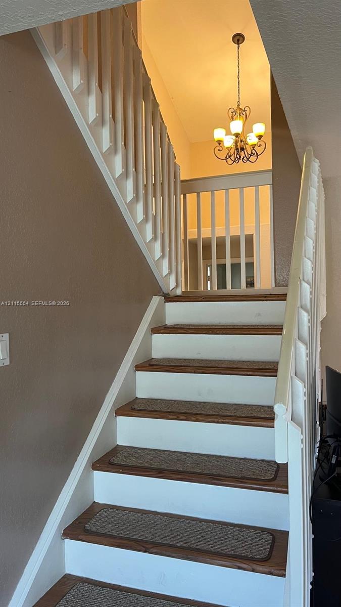 Staircase featuring wood-finish treads, white risers, and white vertical balusters with a matching handrail, complemented by a tiered metal chandelier