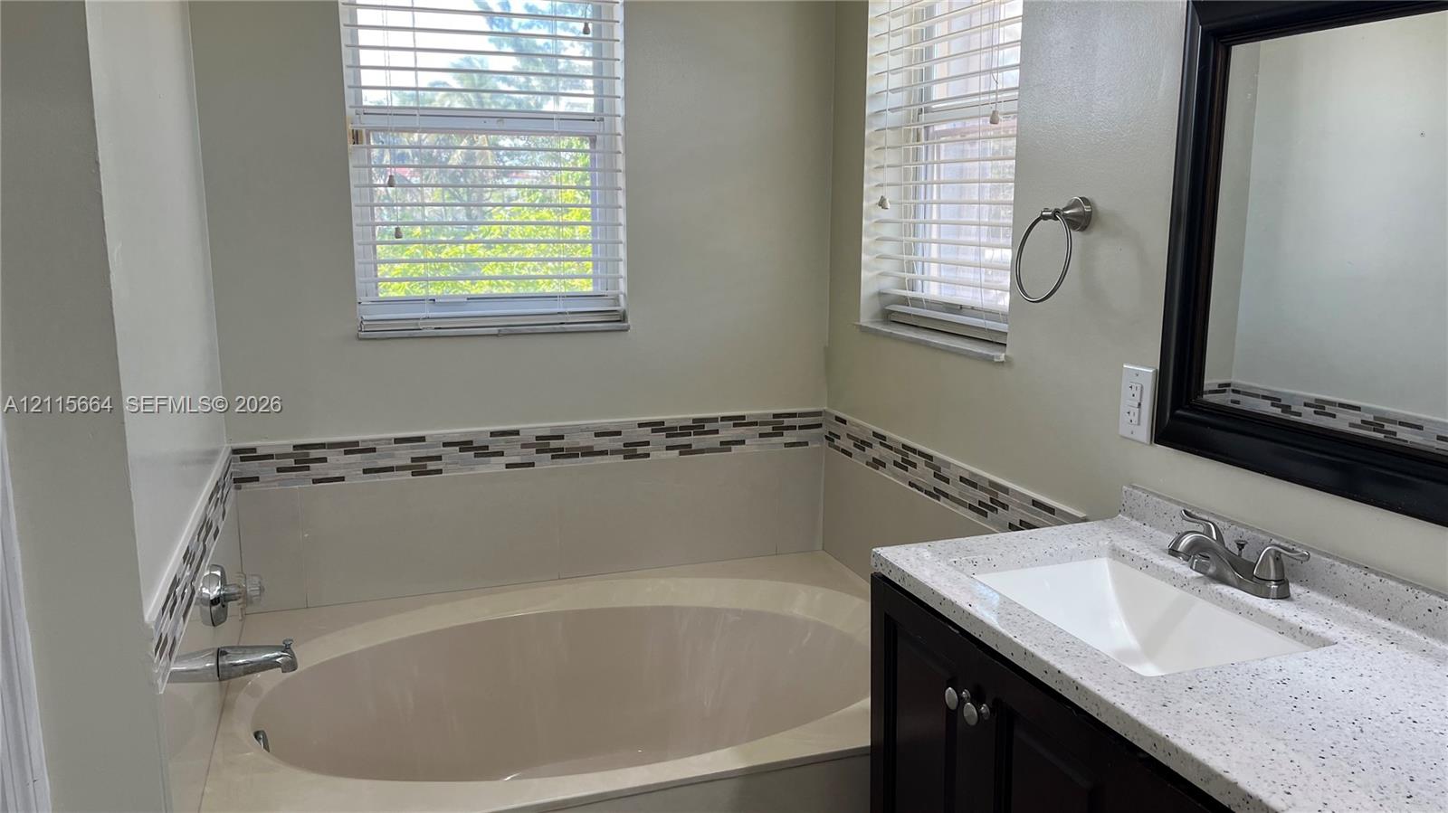 Bathroom featuring a deep soaking tub, dark wood-finish vanity with a stone-composite countertop, undermount sink, and decorative tile backsplash