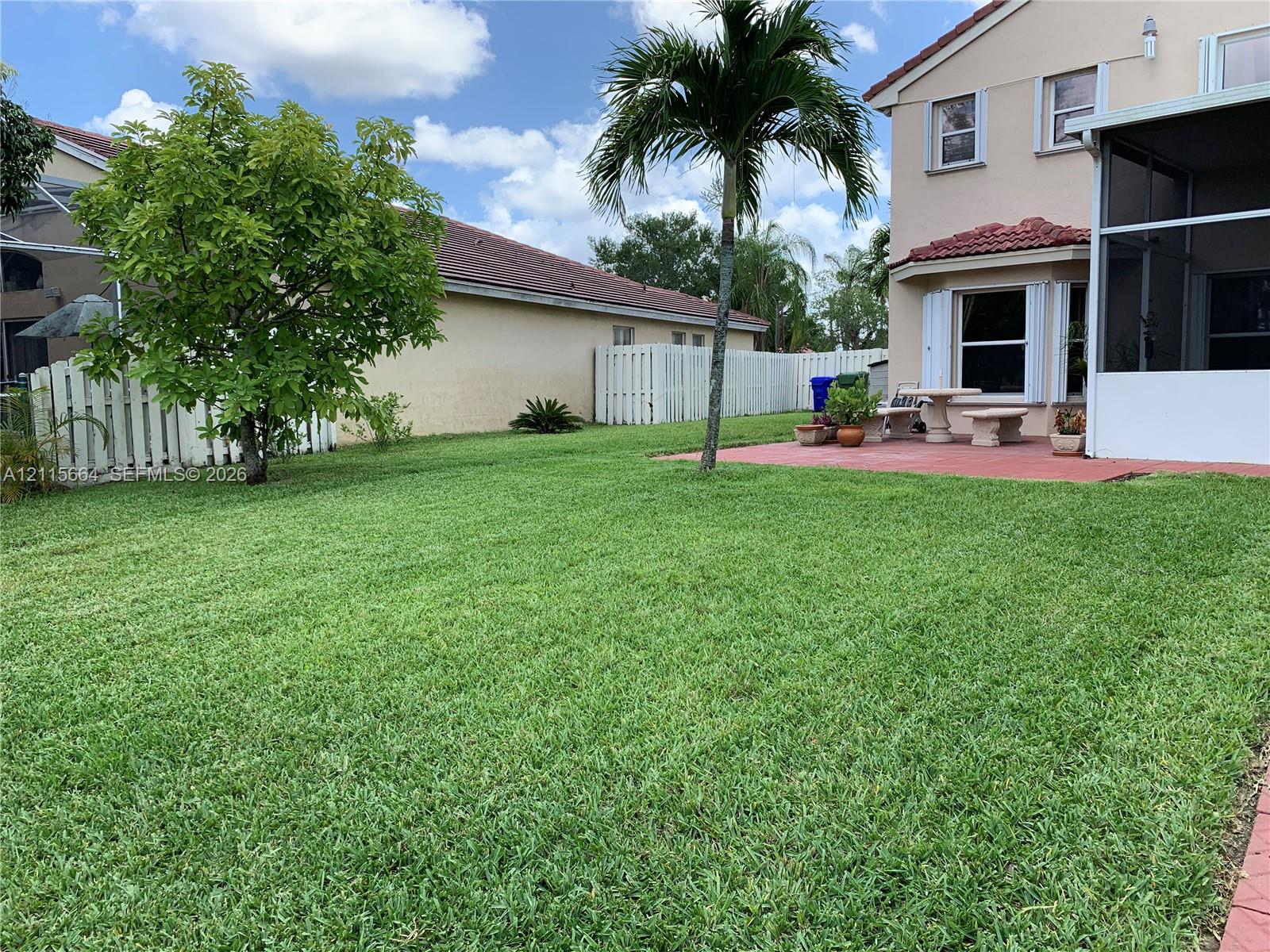 Backyard featuring a grass lawn, paved patio, perimeter vinyl fencing, and mature palm tree