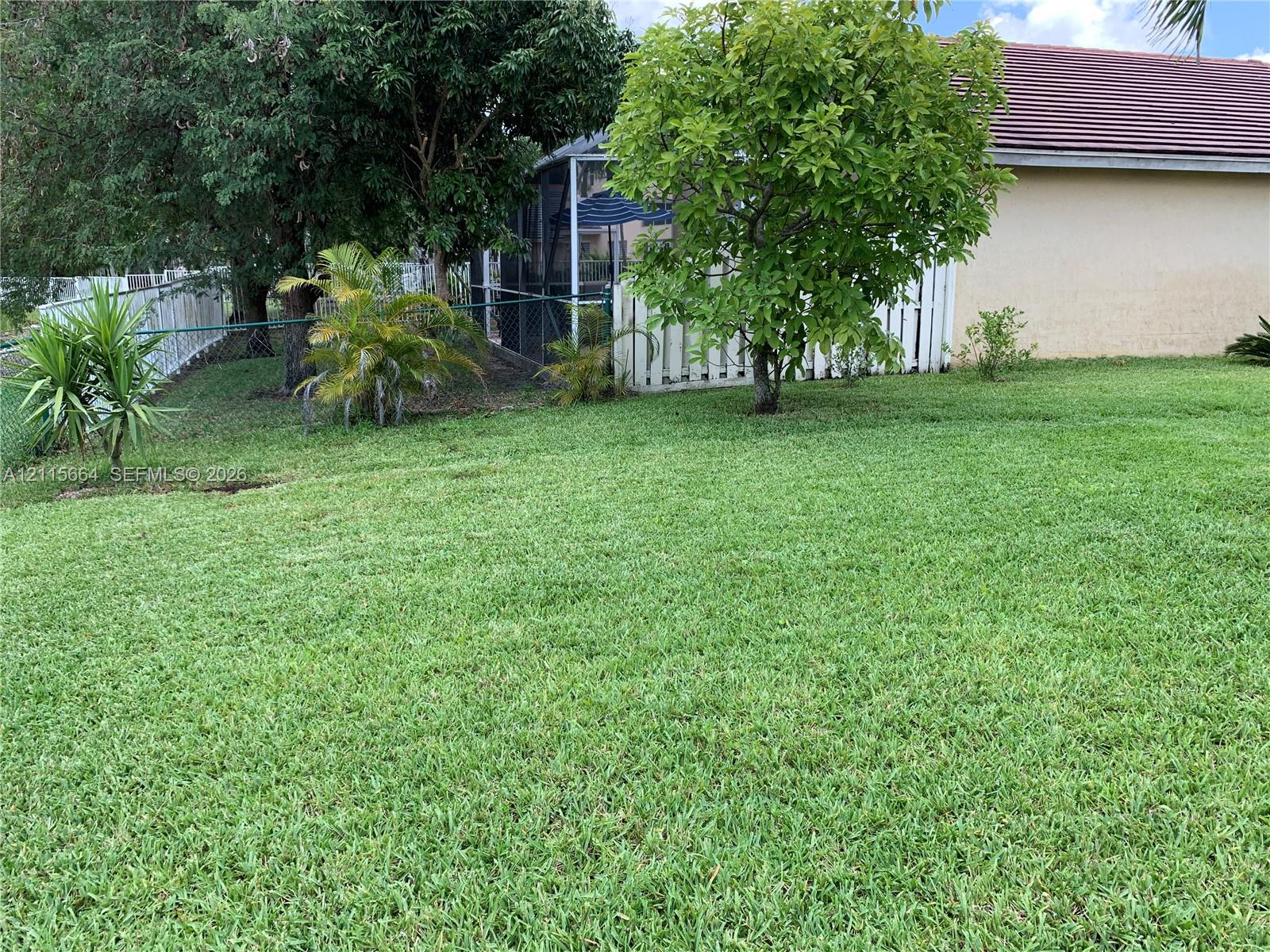 Expansive lawn featuring mature trees, a screened-in enclosure, and white vinyl perimeter fencing