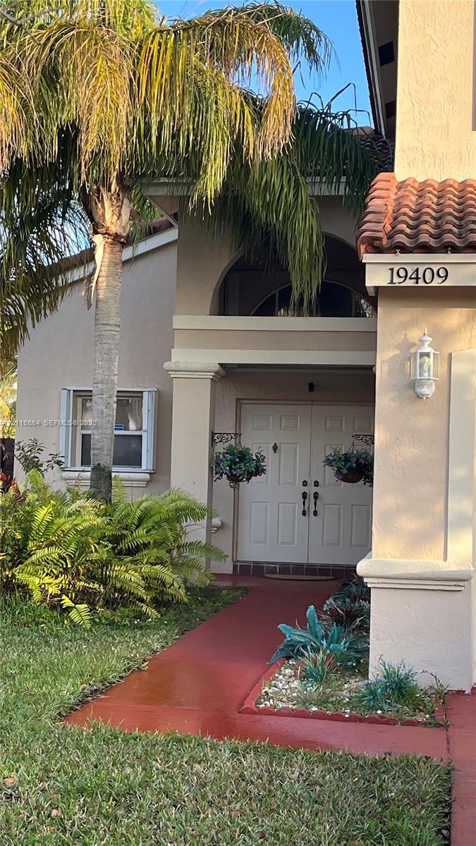 Stucco exterior featuring an arched entryway, double front doors, tile roofing, and a dedicated walkway