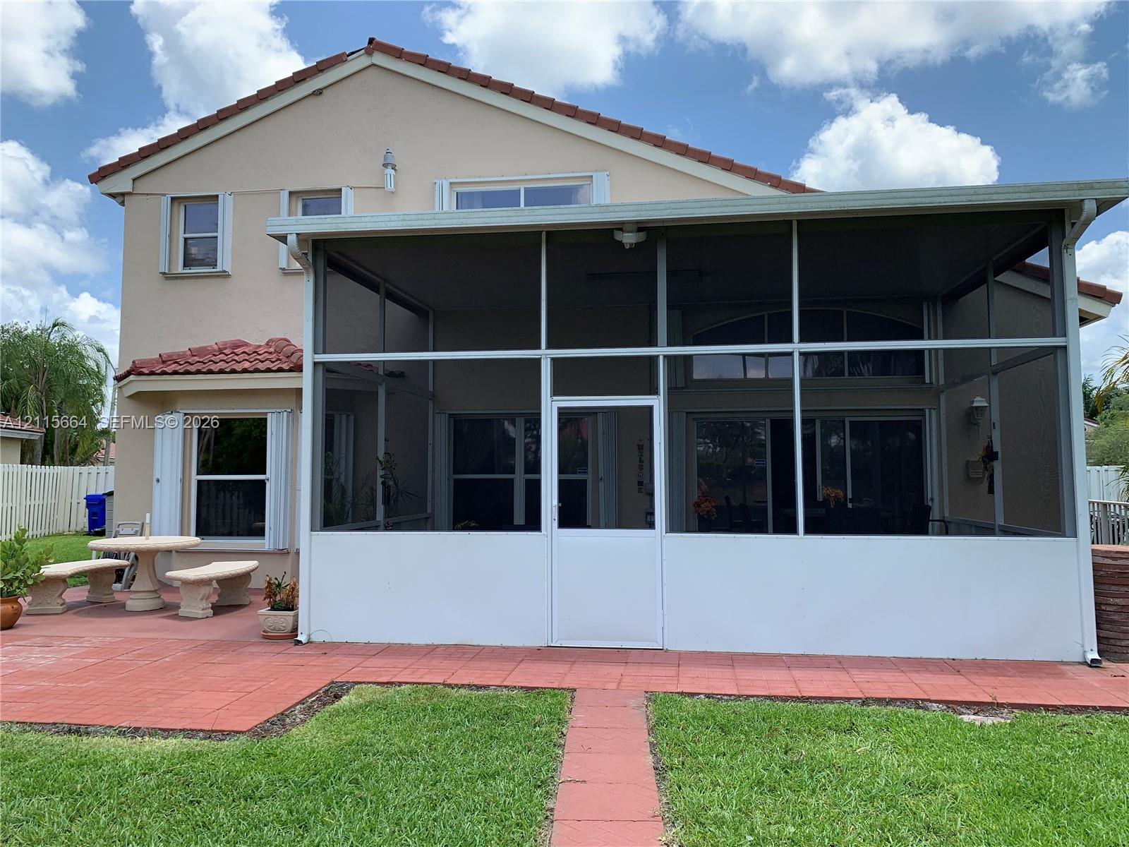 Two-story exterior featuring a screened-in lanai, tile patio, and clay-tile roof