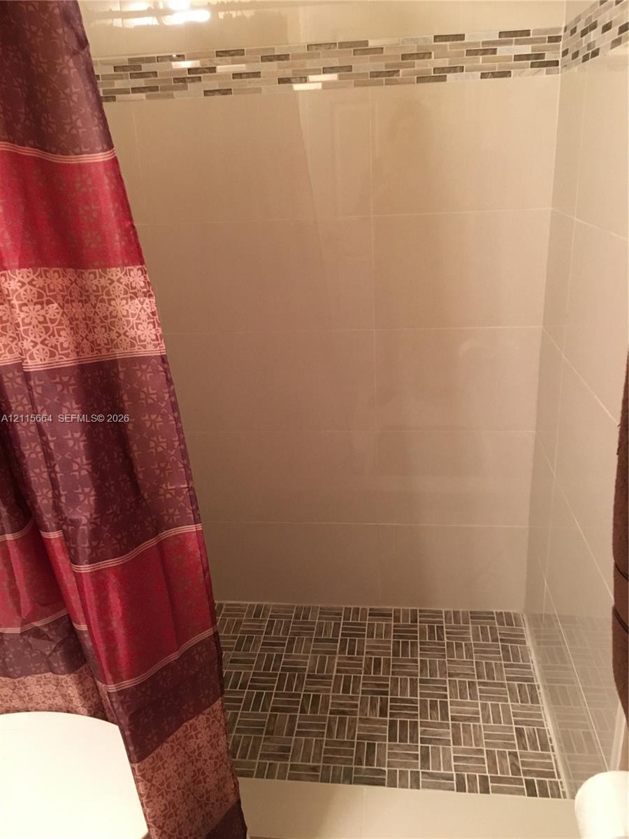 Shower stall featuring large-format wall tile, a textured stone-finish floor, and a decorative tile accent border