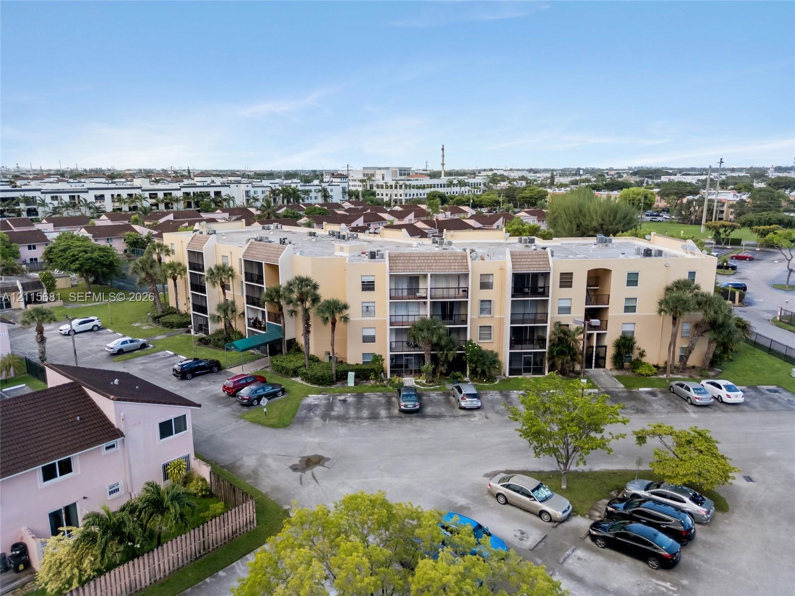 Multi-story residential complex featuring stucco exterior walls, private balconies, a flat roofline, and paved surface parking