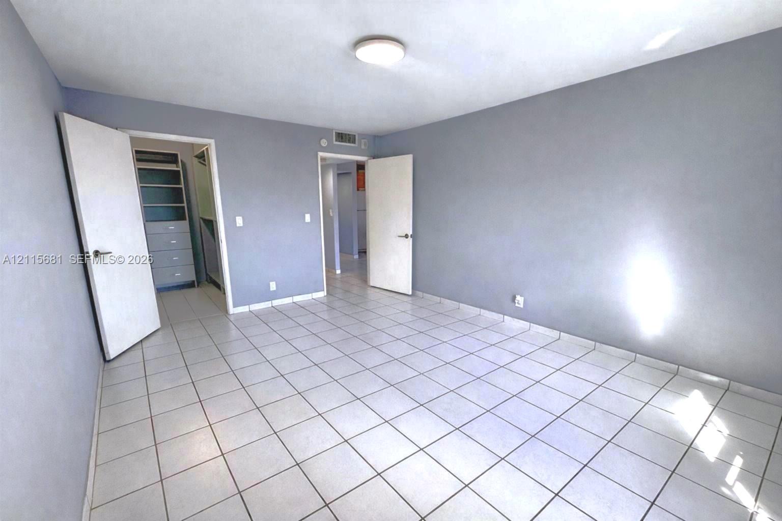 Room featuring light-toned tile flooring, neutral wall paint, and a built-in closet with integrated shelving and drawer storage