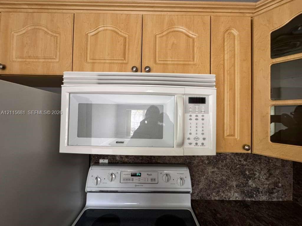 Wood-finish cabinetry featuring recessed-panel doors and glass-front upper storage, paired with an over-the-range microwave and stone-patterned backsplash