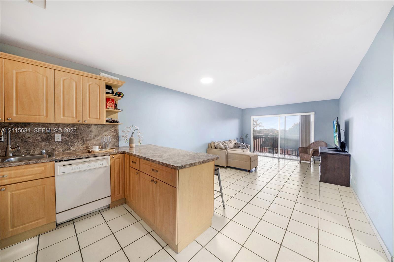 Kitchen featuring light wood-finish cabinetry, stone-patterned countertops, an integrated dishwasher, and tile flooring throughout