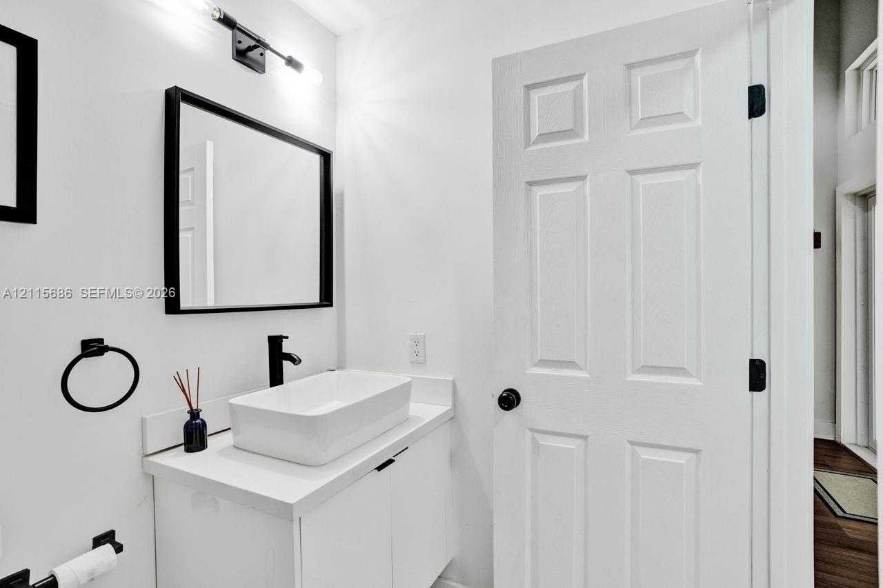White vanity with a rectangular vessel sink, matte black faucet, framed mirror, and coordinating matte black hardware