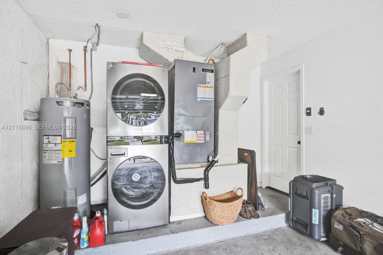 Utility area featuring a stacked stainless steel laundry unit, a vertical water heater, and an integrated climate control system