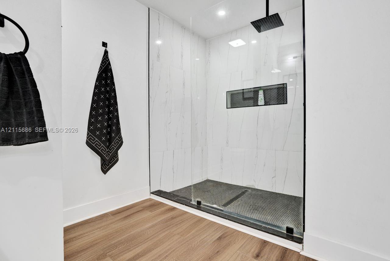 Walk-in shower featuring floor-to-ceiling stone-finish wall tile, frameless glass enclosure, matte black rainfall showerhead, recessed wall niche, and hex-pattern floor tile