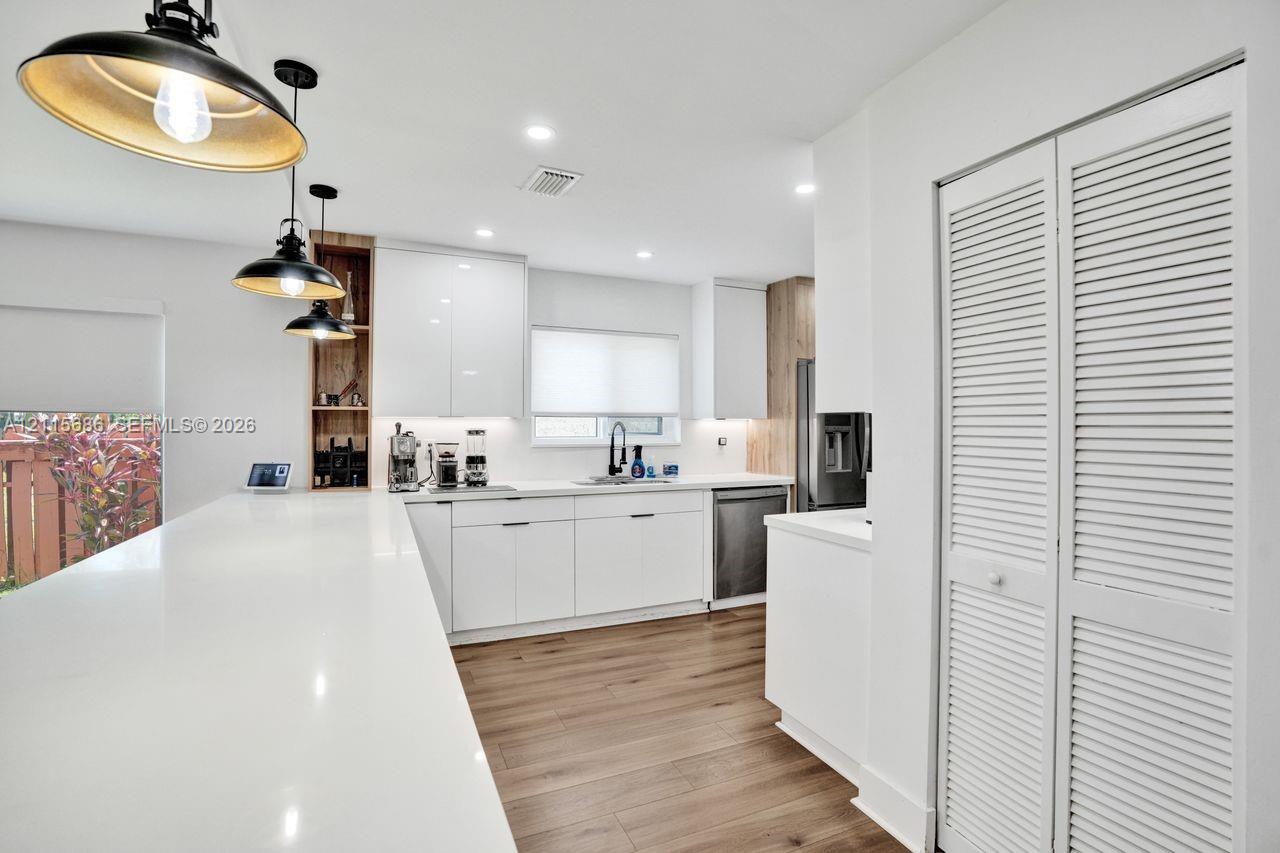 Kitchen featuring white cabinetry, quartz countertops, wood-finish flooring, recessed lighting, and three pendant lights