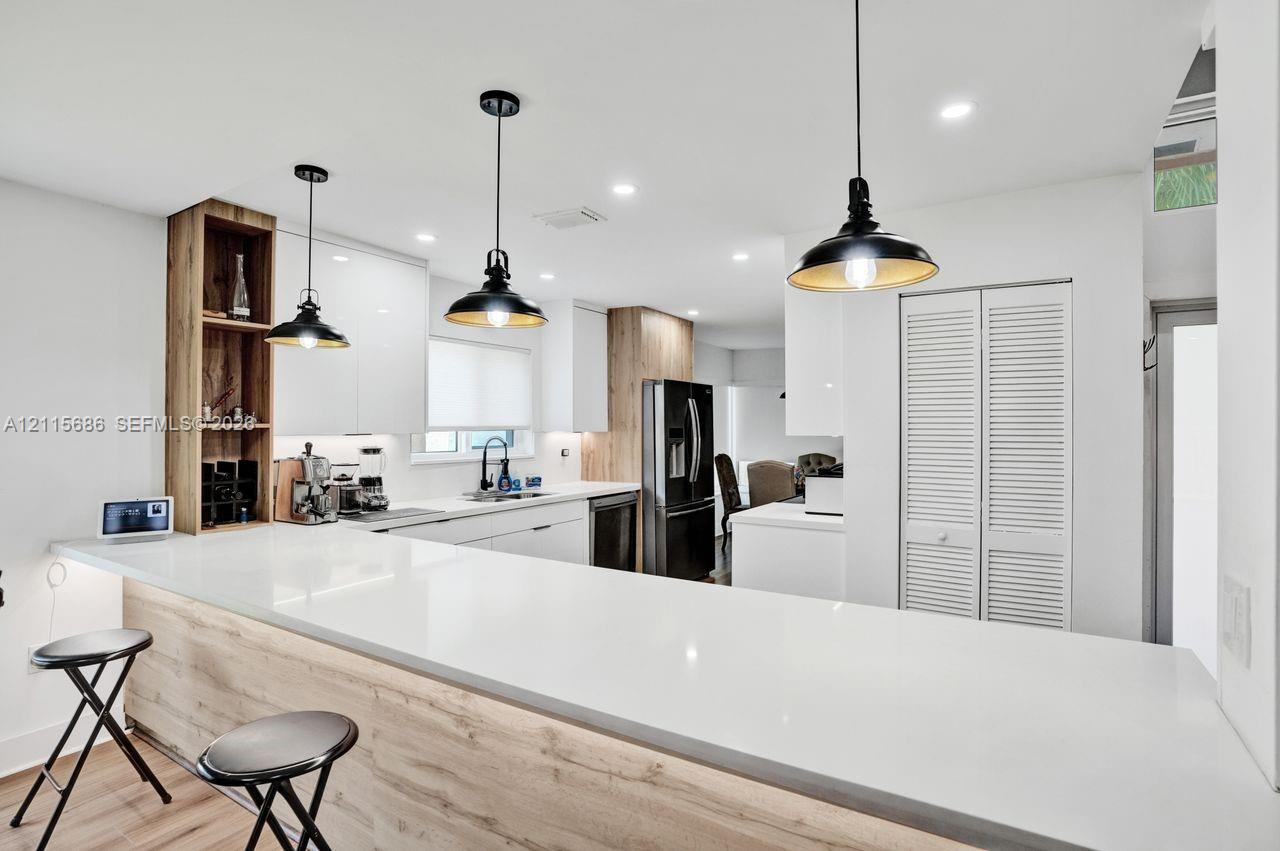 Kitchen featuring white slab-front cabinetry, wood-finish accents, quartz countertops, industrial-style pendant lighting, and recessed ceiling illumination