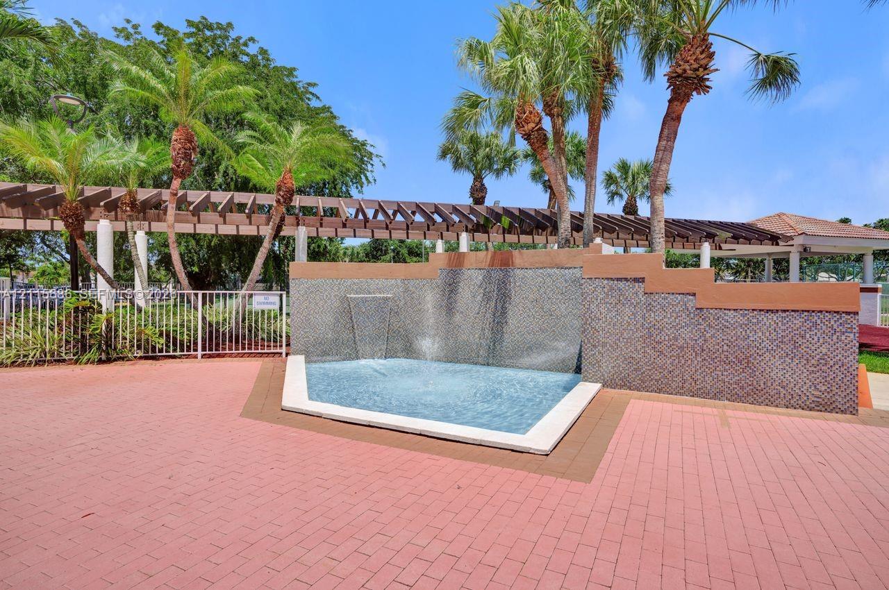 Exterior water feature with tiered stone wall and fountain, paved brick patio, wood-beam pergola, and mature palm trees