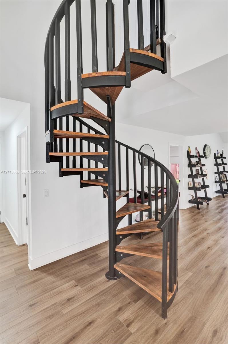 Spiral staircase featuring matte black metal railings and natural wood-finish treads, set against wood-finish flooring