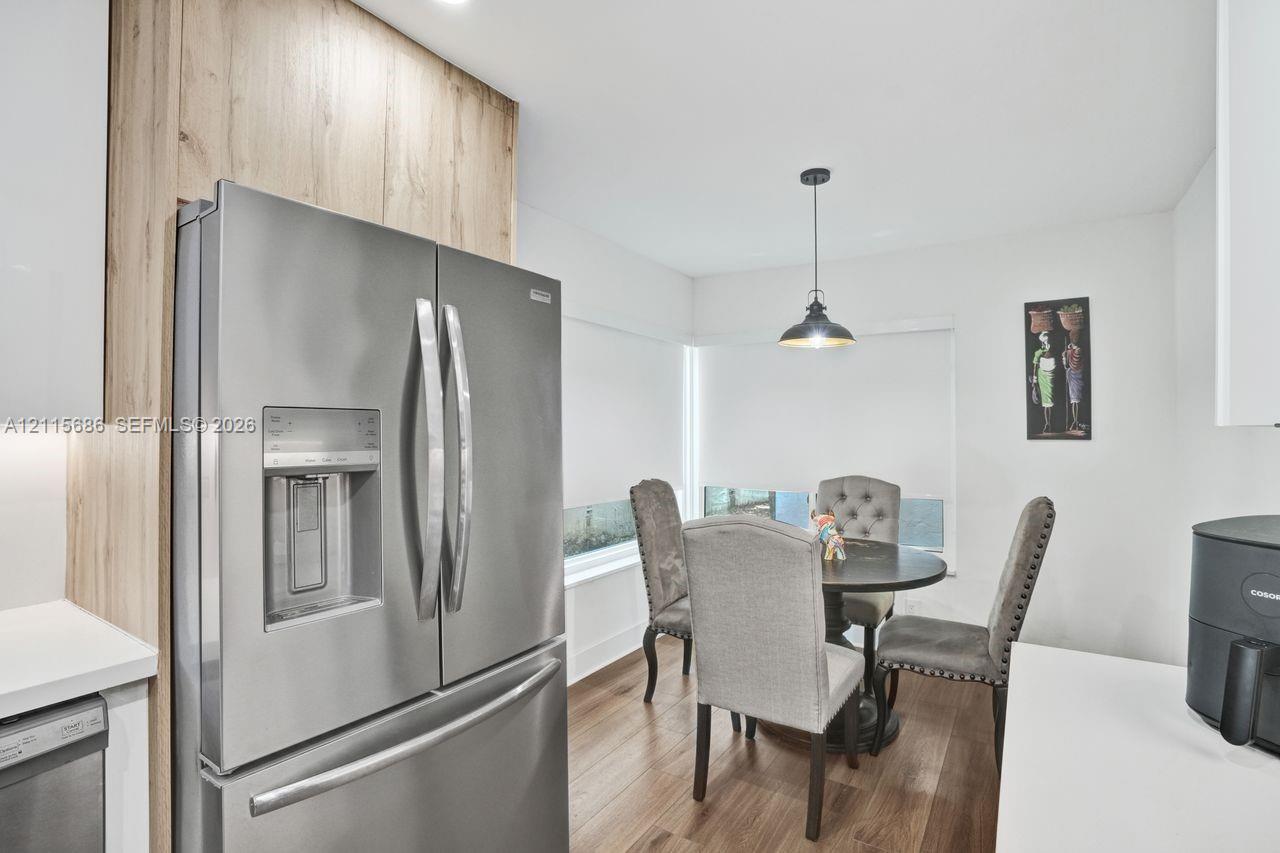 Stainless steel French-door refrigerator, wood-finish cabinetry panels, wood-finish flooring, and industrial-style pendant lighting