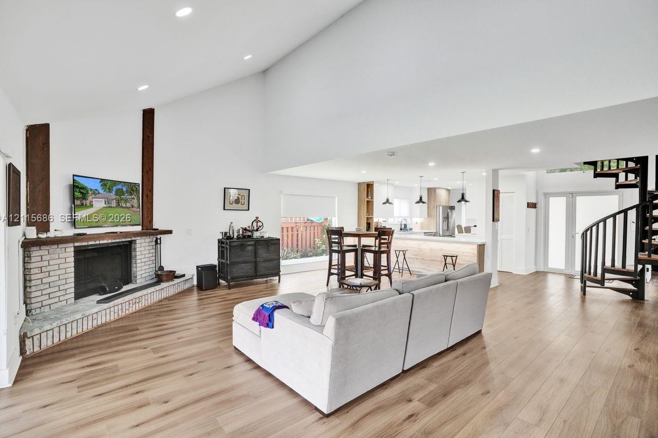 Vaulted ceilings with wood-finish flooring, brick-faced fireplace with prominent wood support beams, spiral staircase, and recessed lighting