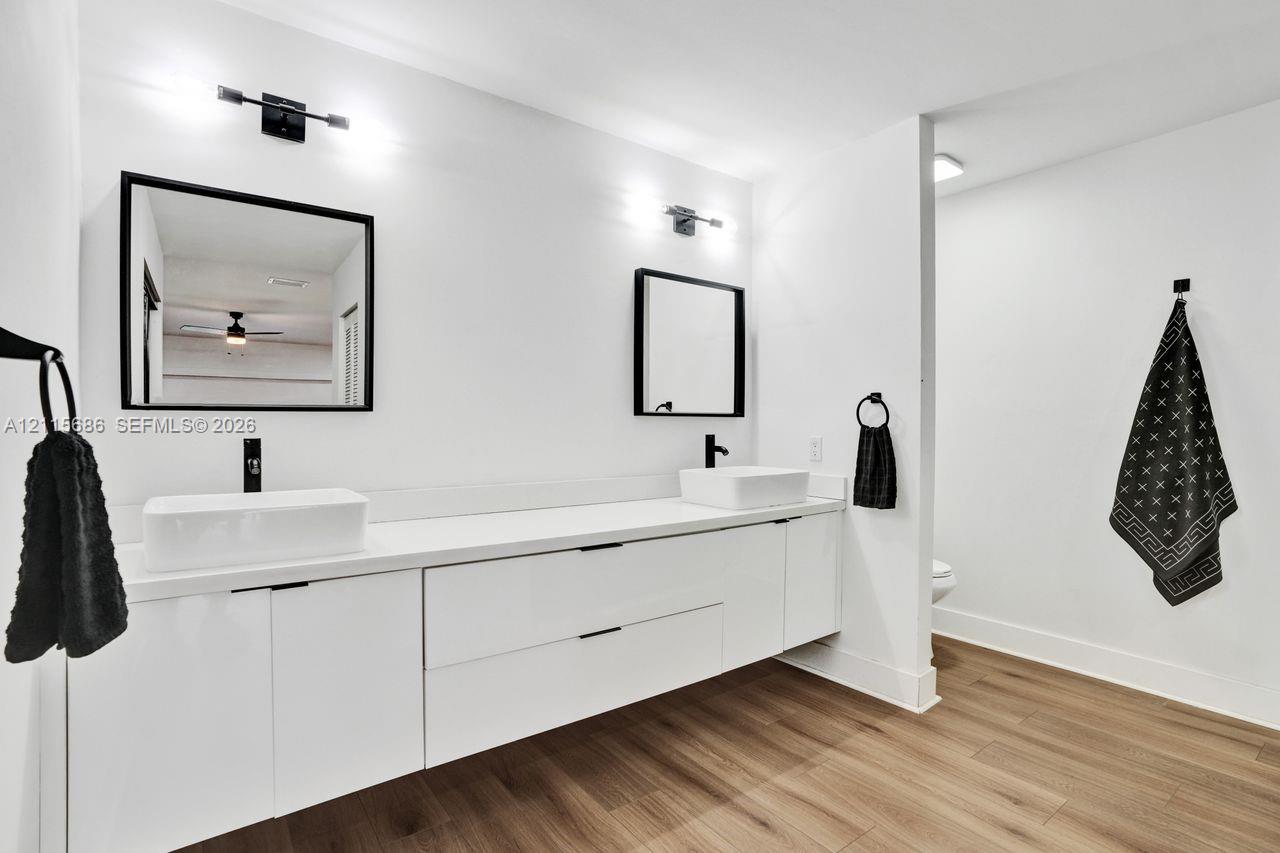 Floating double vanity with rectangular vessel sinks, matte black fixtures, framed mirrors, and wood-finish flooring