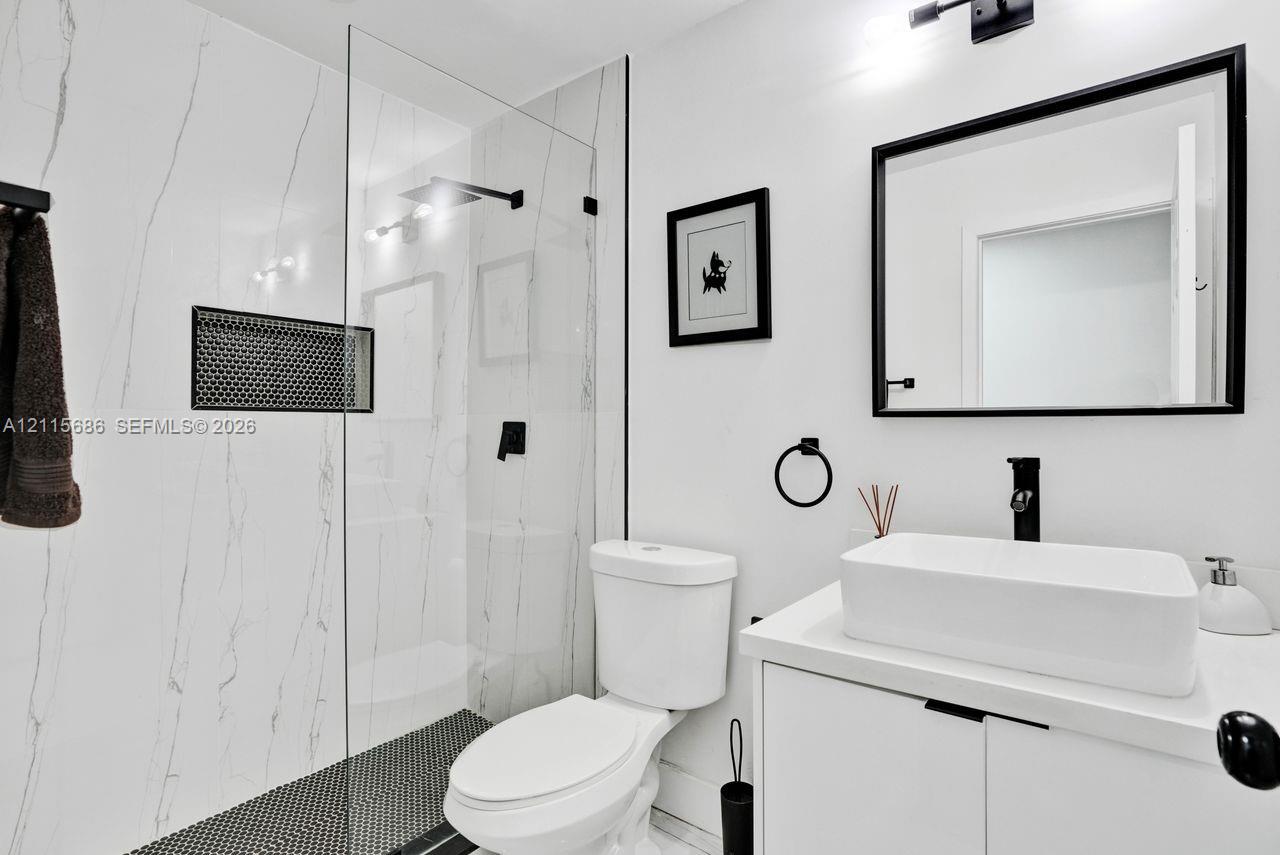 Bathroom featuring a walk-in shower with a frameless glass enclosure, a built-in recessed niche, a modern vanity with a rectangular vessel sink, and matte black fixtures