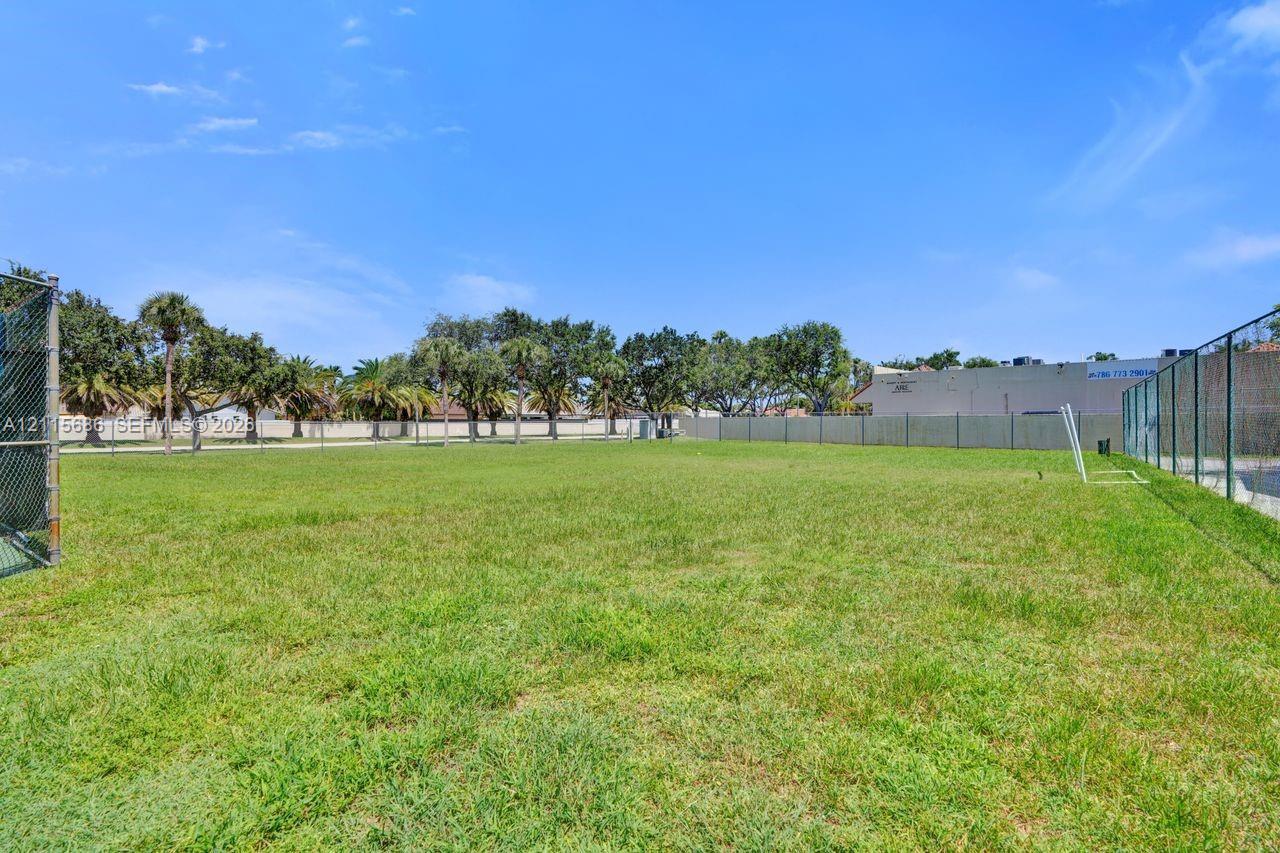 Expansive open-space grounds featuring perimeter chain-link fencing, mature palm trees, and level grass terrain