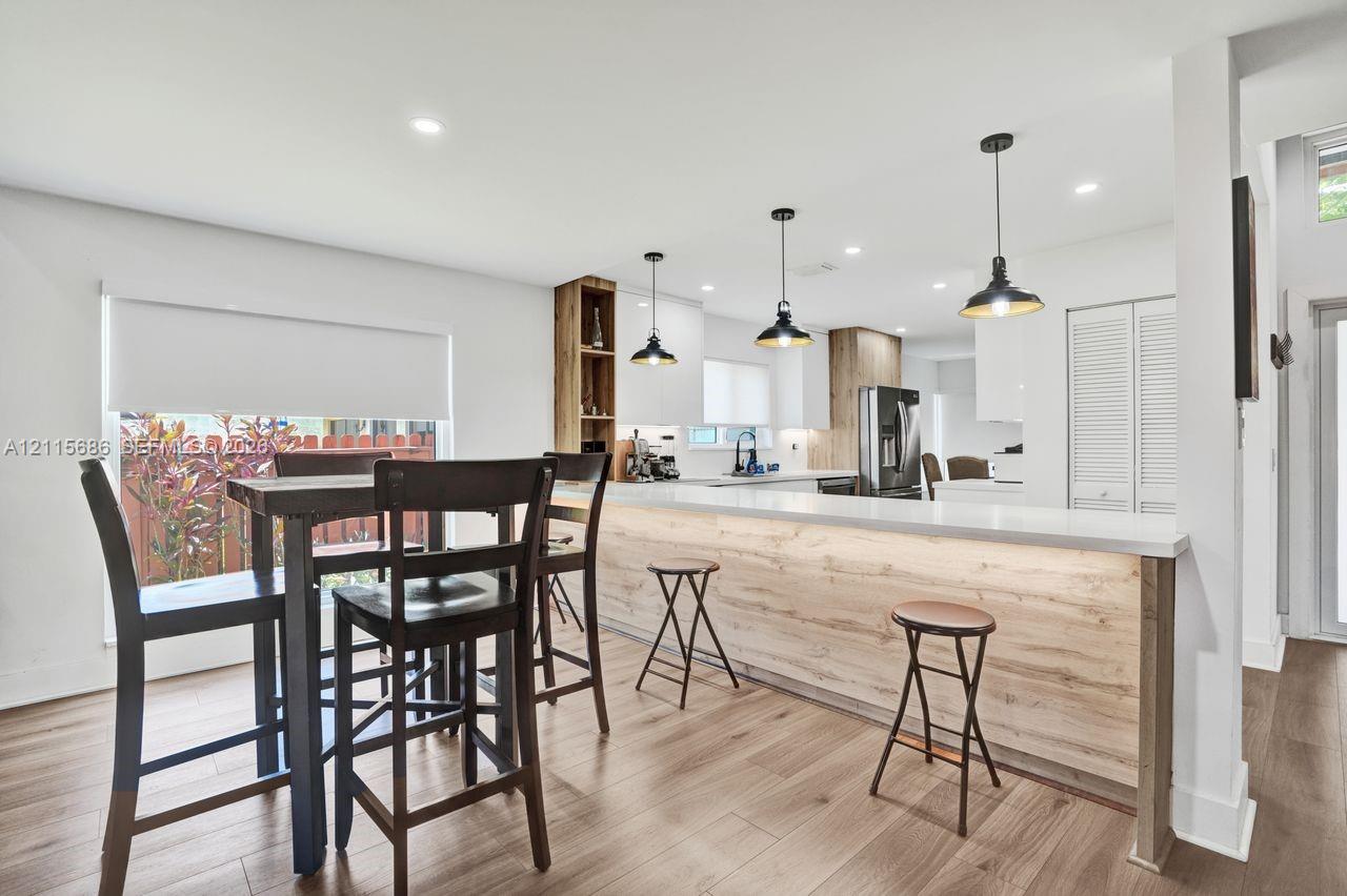 Kitchen featuring a wood-finish island with integrated lighting, wood-finish flooring, recessed ceiling lighting, three pendant lights, and white cabinetry