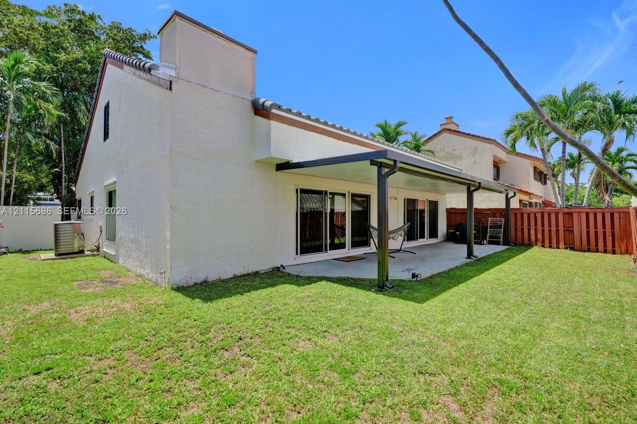 Rear exterior featuring a covered patio, concrete flooring, sliding glass doors, and a wood privacy fence