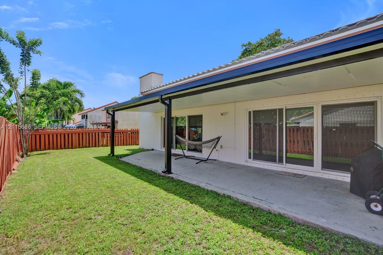 Covered concrete patio with metal support columns, sliding glass doors, and perimeter wood fencing surrounding a grass lawn