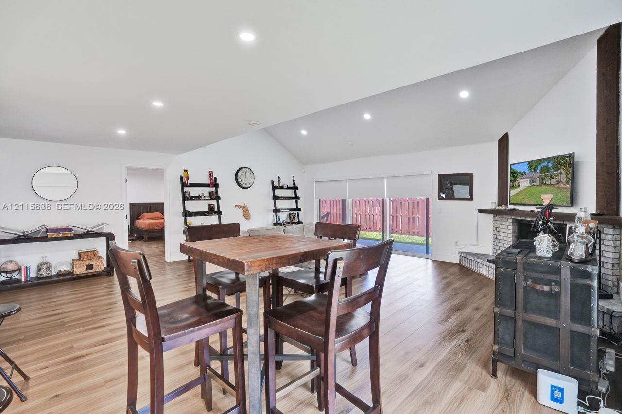 Vaulted ceilings with recessed lighting, wood-finish flooring, and a brick-surround fireplace