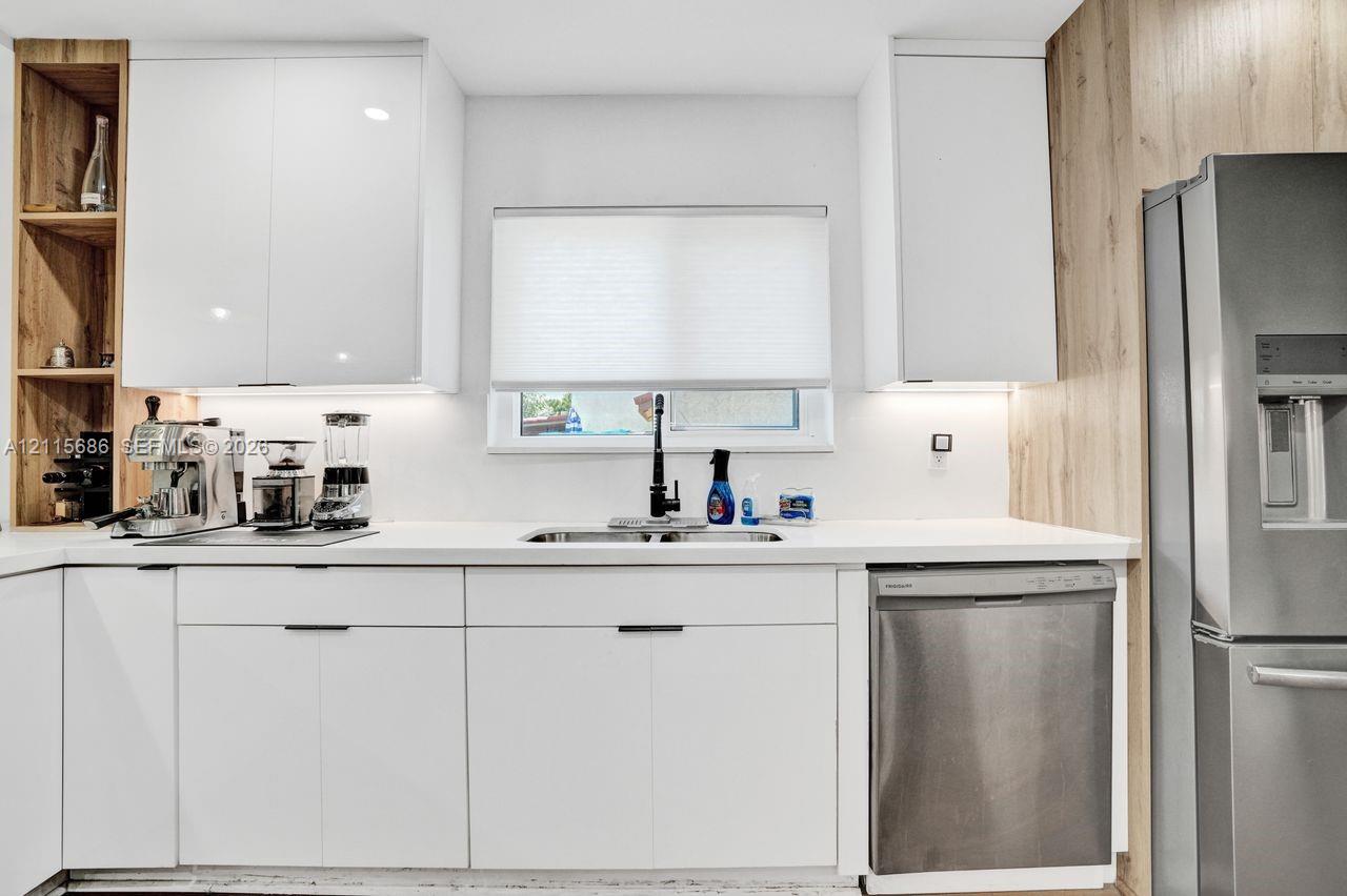 Kitchen featuring white cabinetry, wood-finish shelving, stainless steel appliances, solid surface countertops, and an undermount sink with a high-arch faucet