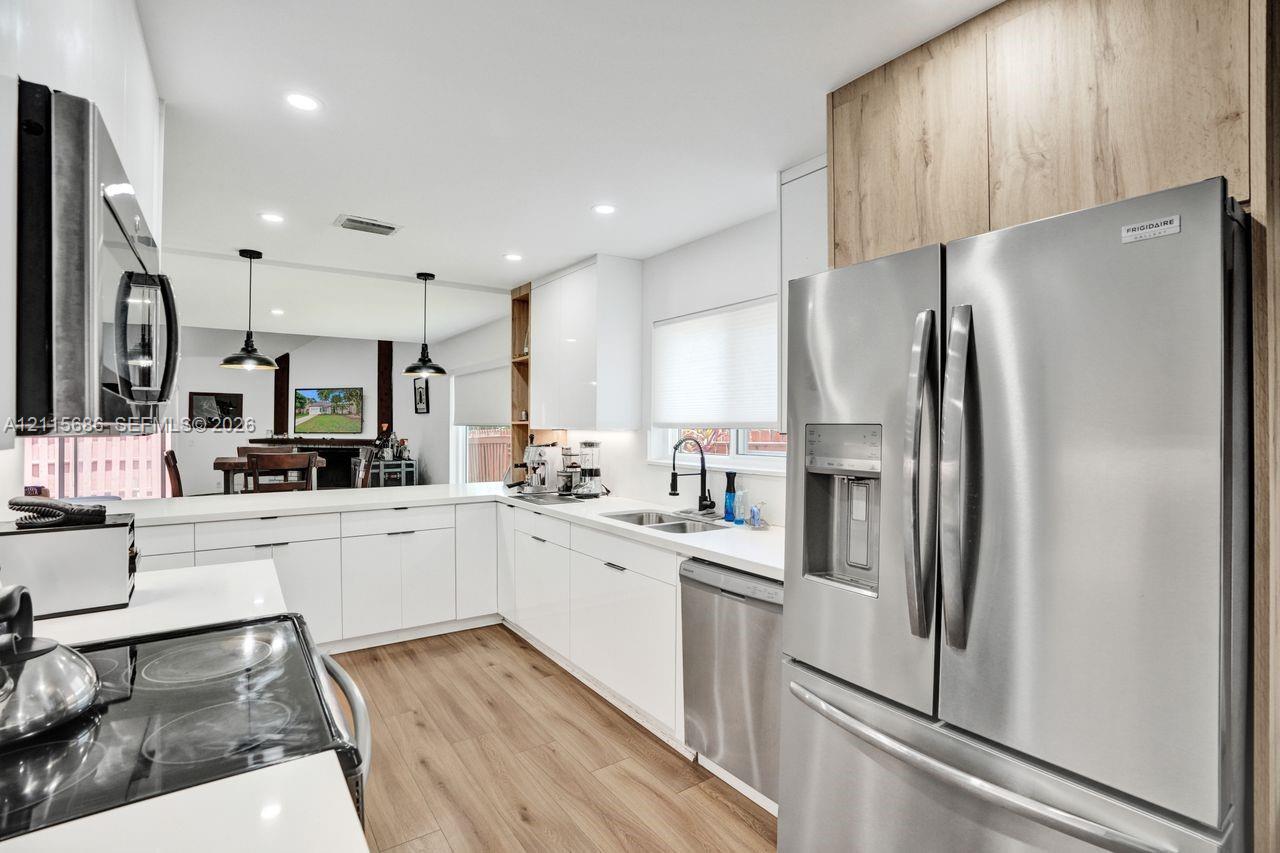 Kitchen featuring high-gloss white cabinetry, stainless steel appliances, wood-finish flooring, recessed lighting, and a neutral solid-surface countertop